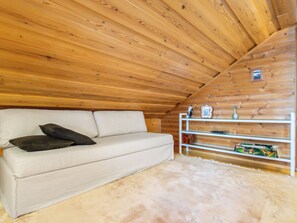 A room with a white sofa, a fluffy rug, wooden ceiling beams, and a white shelf with various items. - Tipuniemi by Interhome (Hämeenlinna)