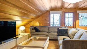 A cozy attic bedroom with wooden walls and a sloped ceiling, featuring a sofa, a TV, and a bedside table. - Tipuniemi by Interhome (Hämeenlinna)