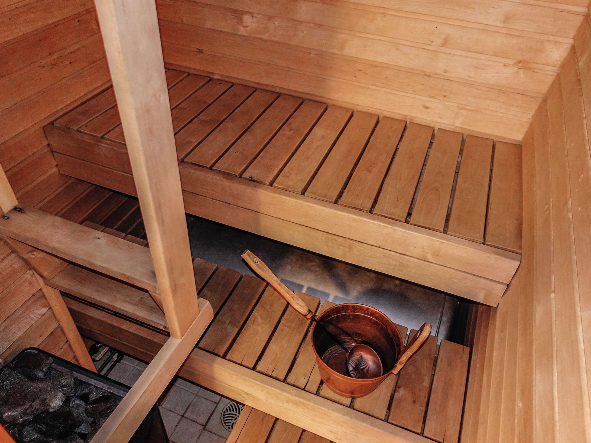 A sauna with wooden benches and a copper bucket.