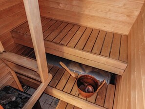 A sauna with wooden benches and a copper bucket.