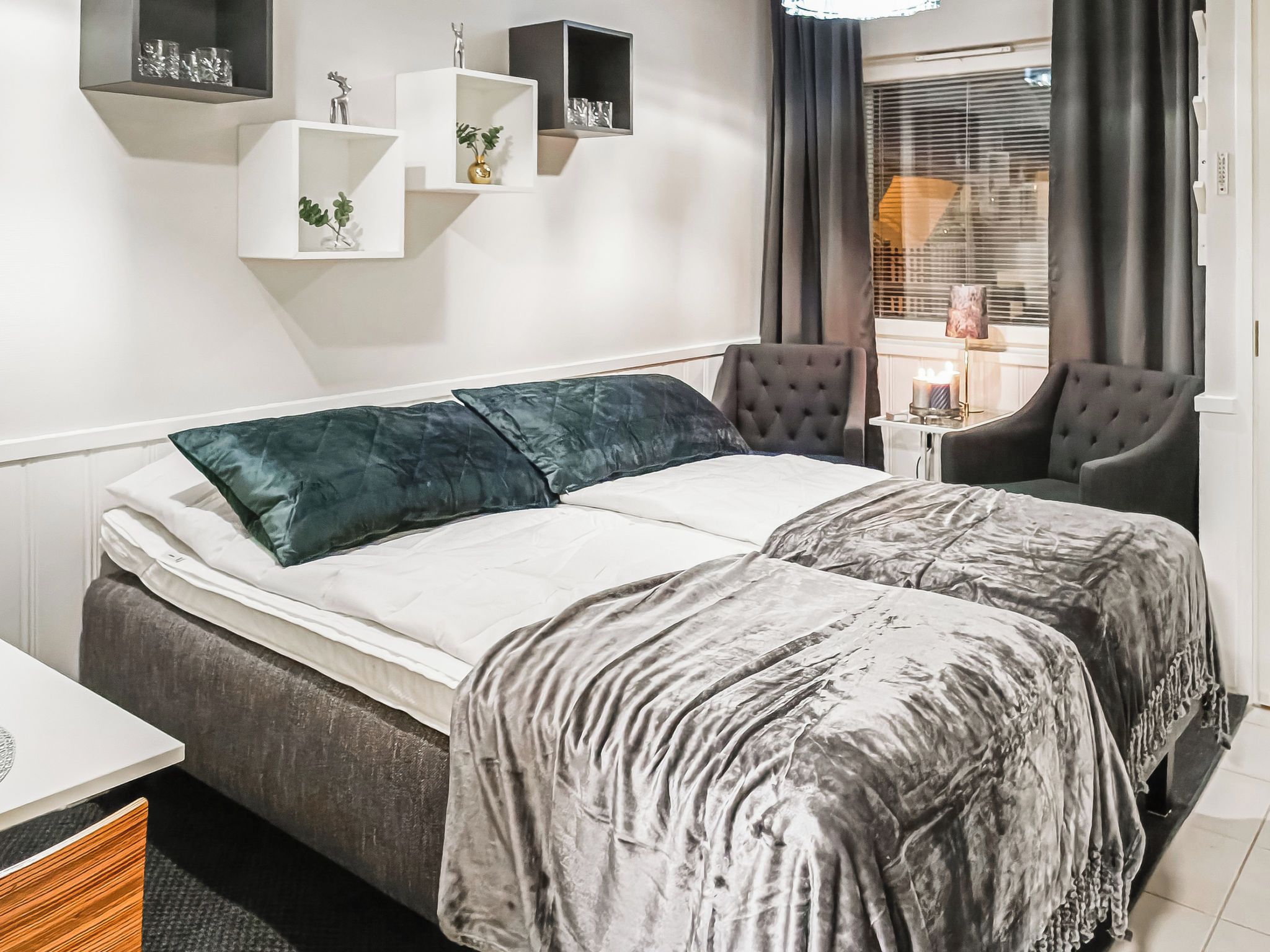 A double bed with a grey and white patterned bedspread, two dark green pillows, and a bedside table with a lamp.