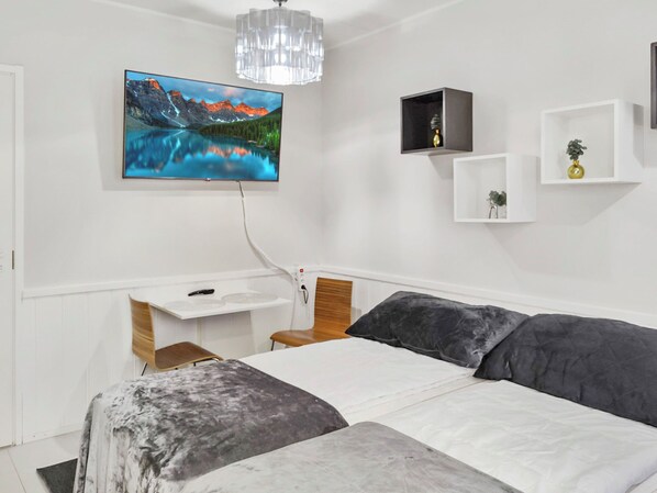 Un dormitorio con cama, escritorio, televisor montado en la pared y candelabro.