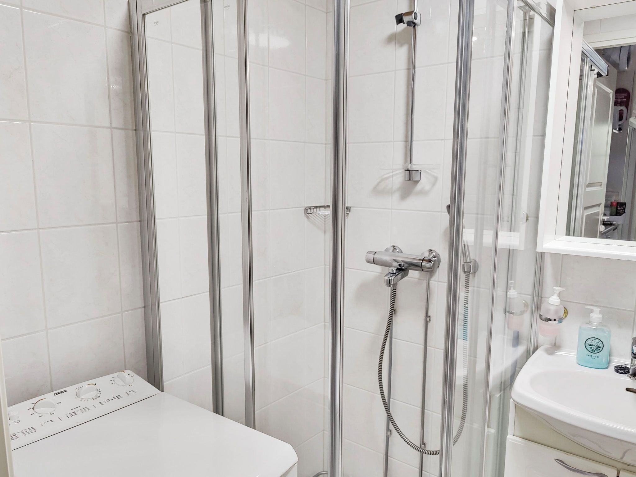 A bathroom with a glass-enclosed shower, a white toilet, and a sink with a mirror above it.