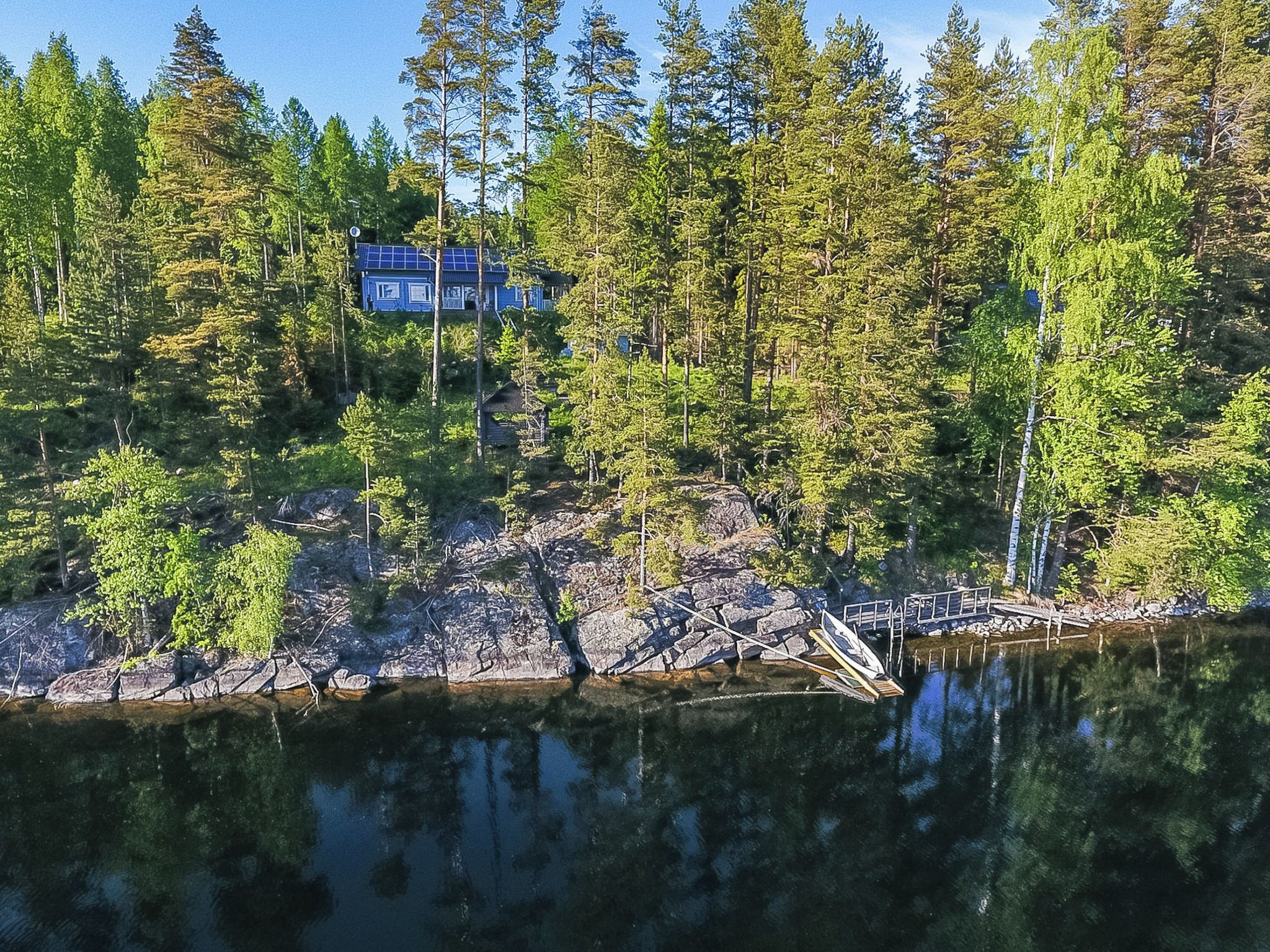 A lakeside cabin surrounded by dense forest, with a dock extending into the water.
