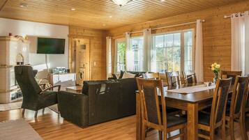 A cozy cabin interior with a wooden ceiling, a dining area with a table and chairs, a sofa, and a television mounted on the wall.