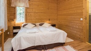 Quarto de cabana de madeira com uma cama, uma janela e uma mesinha de cabeceira.