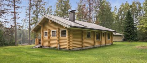 A log cabin with a chimney, a porch, and a view of the surrounding forest.