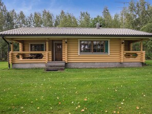 Une cabane en rondins avec un porche, une porte d’entrée et une fenêtre.