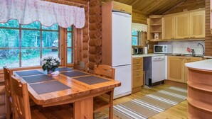 A wooden cabin with a dining table, chairs, a refrigerator, a microwave, and a sink in the kitchen.
