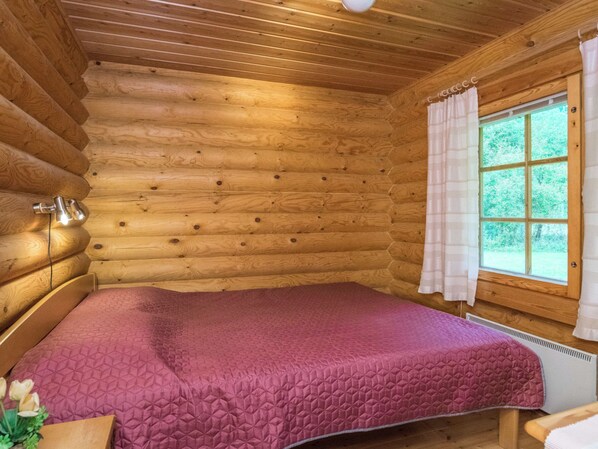 A log cabin room with a bed, a window with curtains, and a wall-mounted light fixture. - Uitonniemi, rummukkala by Interhome (Heinävesi)