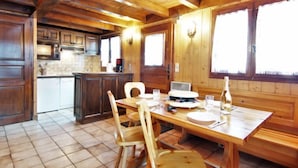 A wooden cabin interior with a kitchen and dining area, featuring a wooden table, chairs, and a large window. - Pierre Blanche by Interhome (Les Houches)