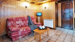 A cozy room with wooden walls and ceiling, a red patterned sofa, a small wooden table with a tray of tea items, and a television on the wall. - Pierre Blanche by Interhome (Les Houches)