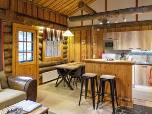 L’intérieur chaleureux d’un chalet en bois comprend une table à manger en bois, des tabourets de bar, un canapé et un coin cuisine équipé d’un four à micro-ondes.
