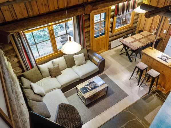 A cozy log cabin interior with a sofa, dining table, and large windows.