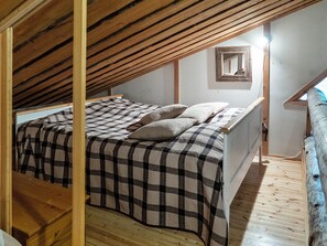 Une chambre avec un plafond en pente, un lit recouvert d’une couverture à carreaux et un petit miroir accroché au mur.