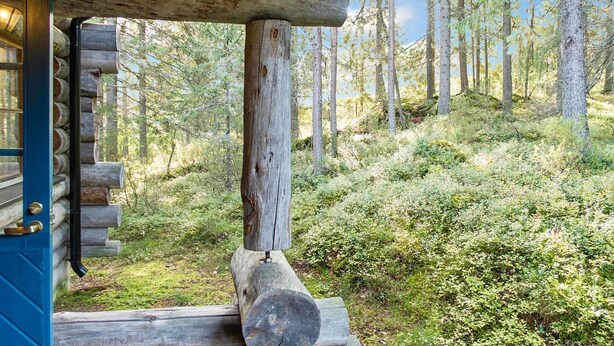 A log cabin with a porch overlooking a forested hillside.