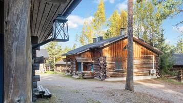 Une cabane rustique en rondins de bois, dotée d’une véranda, d’un banc et offrant une vue dégagée sur la forêt environnante.