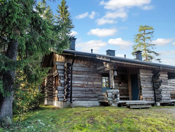 Une cabane en rondins avec un porche à l’avant, une cheminée et une fenêtre.
