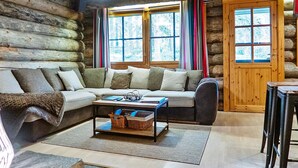 A log cabin interior with a sofa, a coffee table, and a window with curtains.