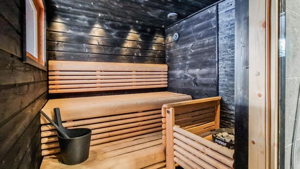 Eine Sauna mit Holzbänken und einer schwarzen Heizvorrichtung.