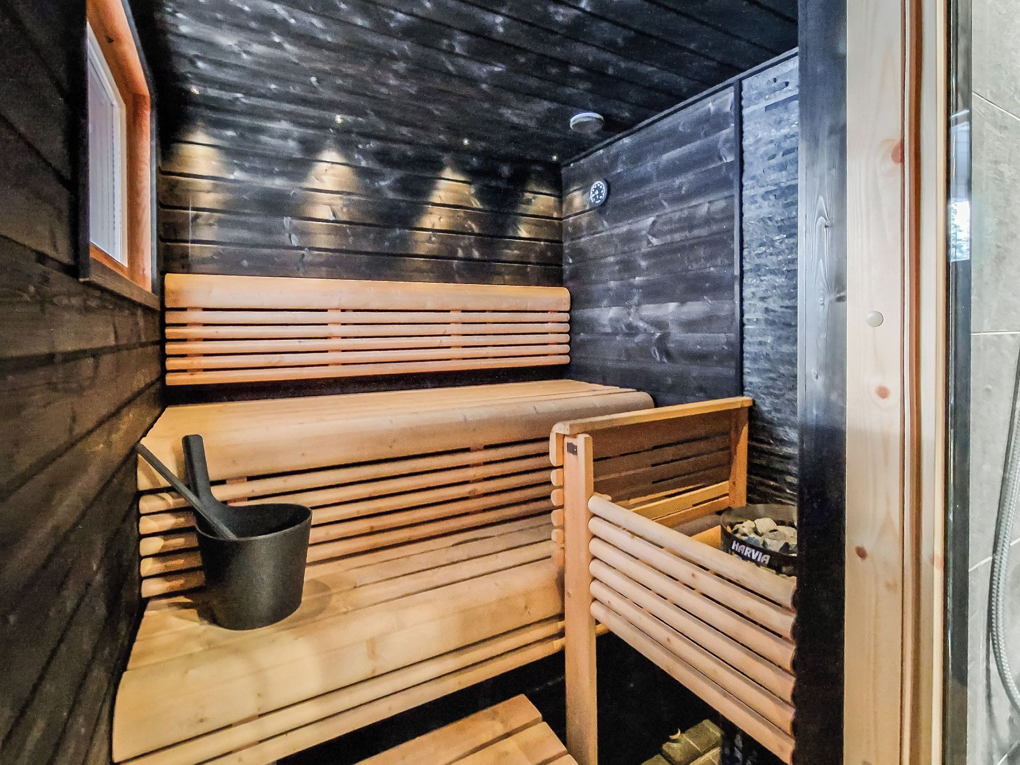 Una sala de sauna con bancos de madera y un cubo negro.