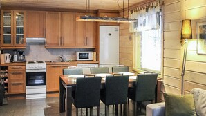 Eine kleine Küche mit Holzausstattung, einer Mikrowelle, einem Herd und einem Kühlschrank. Im Wohnbereich befindet sich ein Esstisch mit Stühlen und eine Couch.