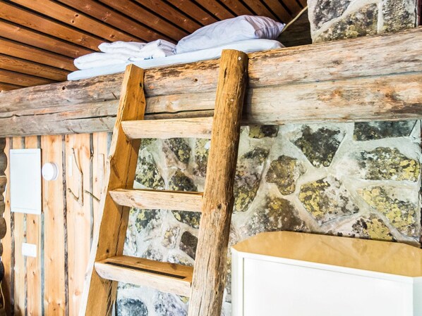 Una escalera de madera apoyada contra una pared de piedra, con un techo de madera rústica y un armario blanco abajo.