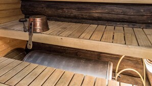 A wooden cabin interior with a metal stove, a shelf with a pot, and a wooden bench. - Tievatupa 2, pienempi by Interhome (Ylläsjärvi)