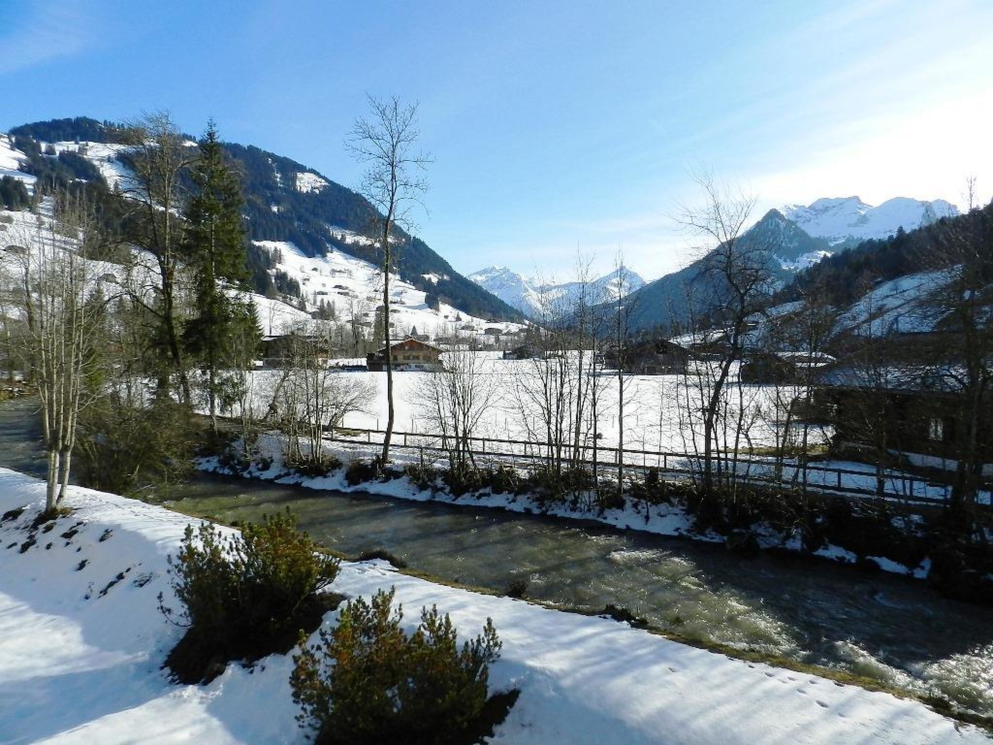 A snow-covered landscape with a river, mountains, and sparse trees.