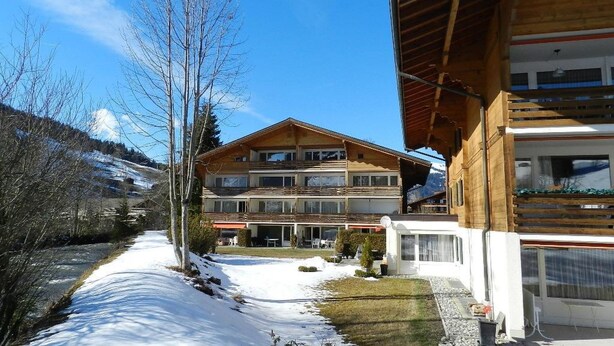 Ein zweistöckiges Holzhaus mit einer Skipiste im Hintergrund.