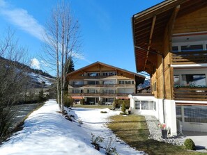 Ein zweistöckiges Holzhaus mit einer Skipiste im Hintergrund.