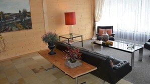 Ein Wohnzimmer mit Holzboden, einem schwarzen Sofa, einem Glastisch, einer roten Stehlampe und einem Gemälde an der Wand.