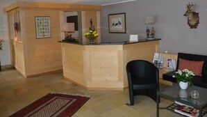 Ein Empfangsbereich mit Holztresen, einem schwarzen Stuhl, einer Couch und einem Couchtisch.