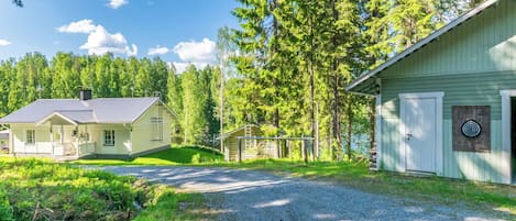 Une maison à deux étages, dotée d’un porche et d’un garage, entourée d’une forêt et bordée d’une allée en gravier.