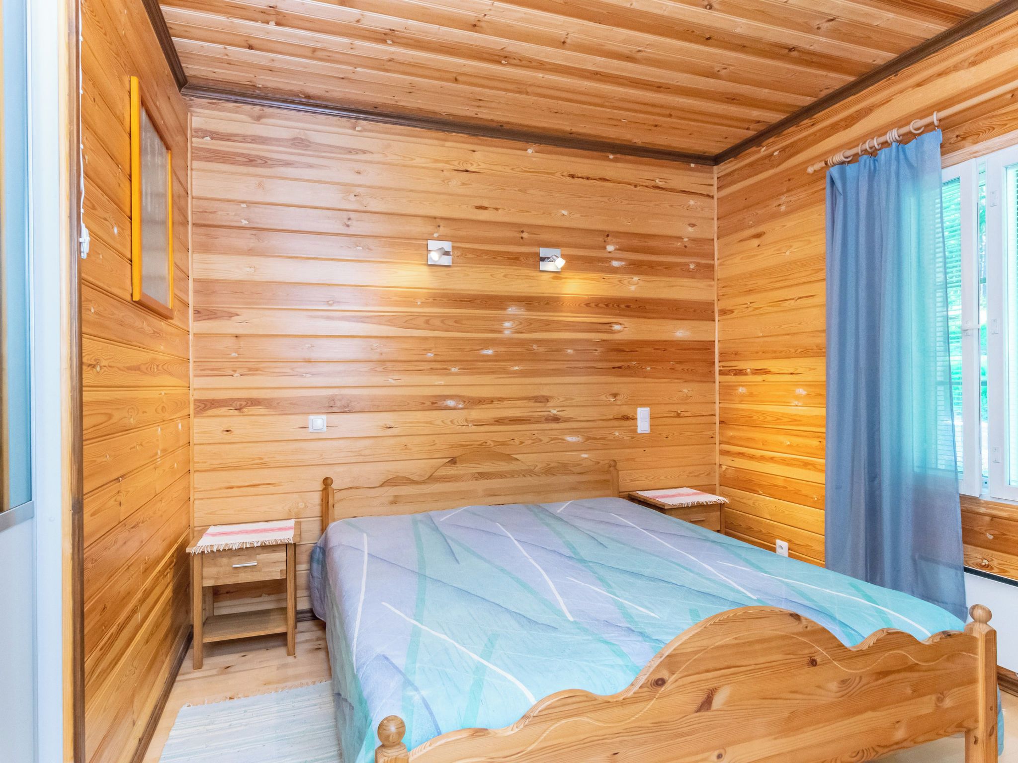 A wooden-paneled room with a bed, two bedside tables, and a window with curtains.
