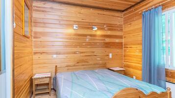 A wooden-paneled room with a bed, two bedside tables, and a window with curtains.