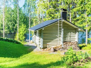 A log cabin with a chimney, surrounded by a grassy area and trees. - Salmenranta by Interhome (Heinävesi)