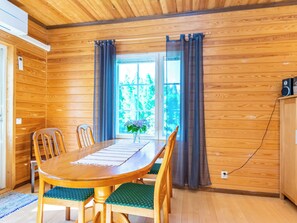 Une pièce aux murs lambrés, comprenant une table à manger, des chaises, une fenêtre avec des rideaux et un haut-parleur posé sur un meuble.