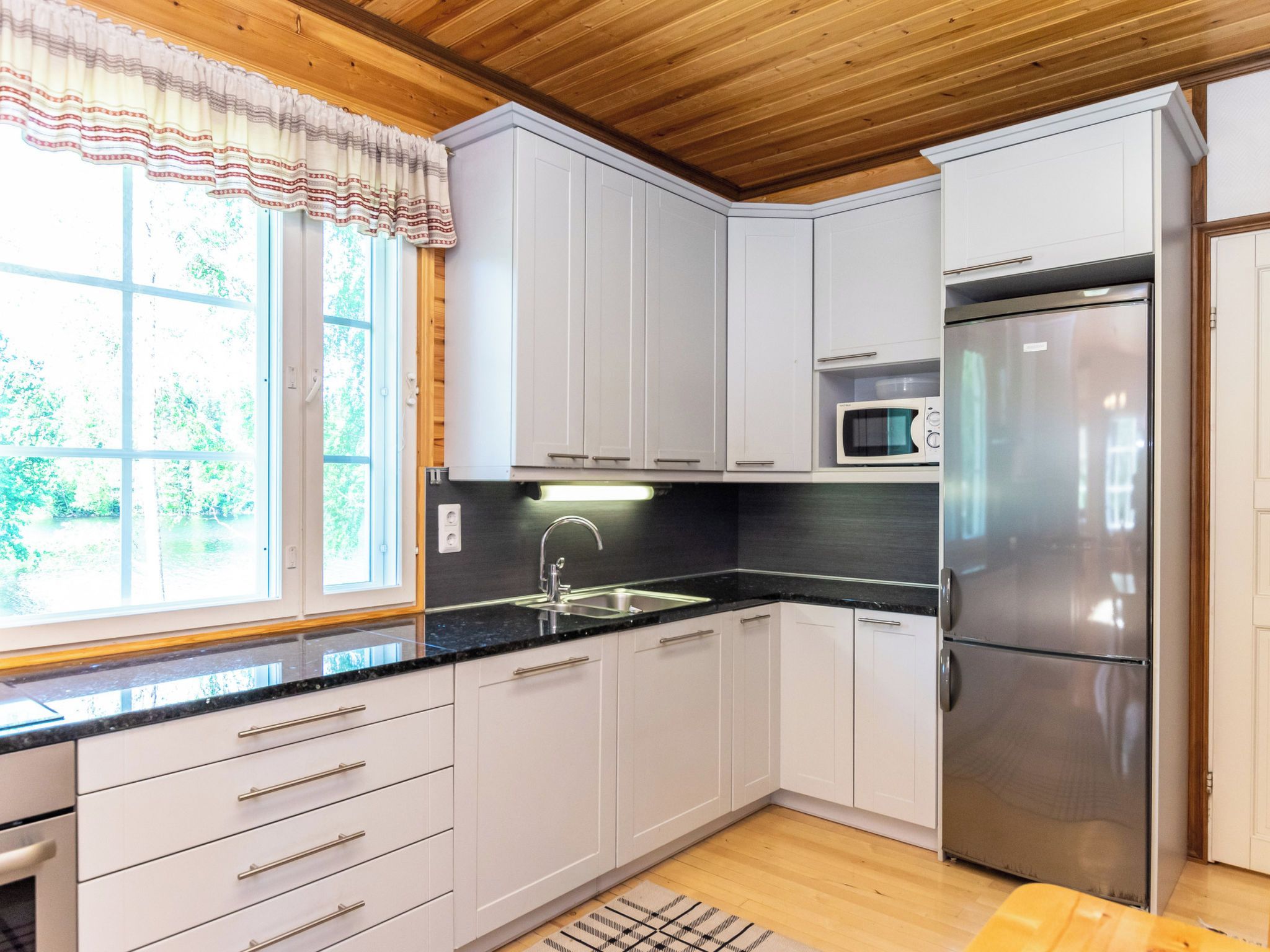 A modern kitchen with white cabinets, a stainless steel refrigerator, a microwave, and a sink with a faucet.