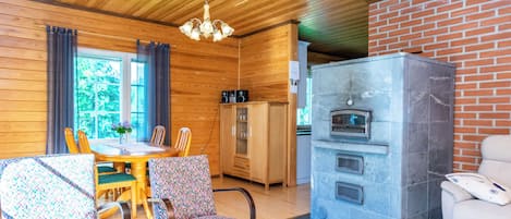 Une pièce chaleureuse avec un plafond en bois, un coin repas avec une table et des chaises, un canapé à motifs et une cheminée en pierre.