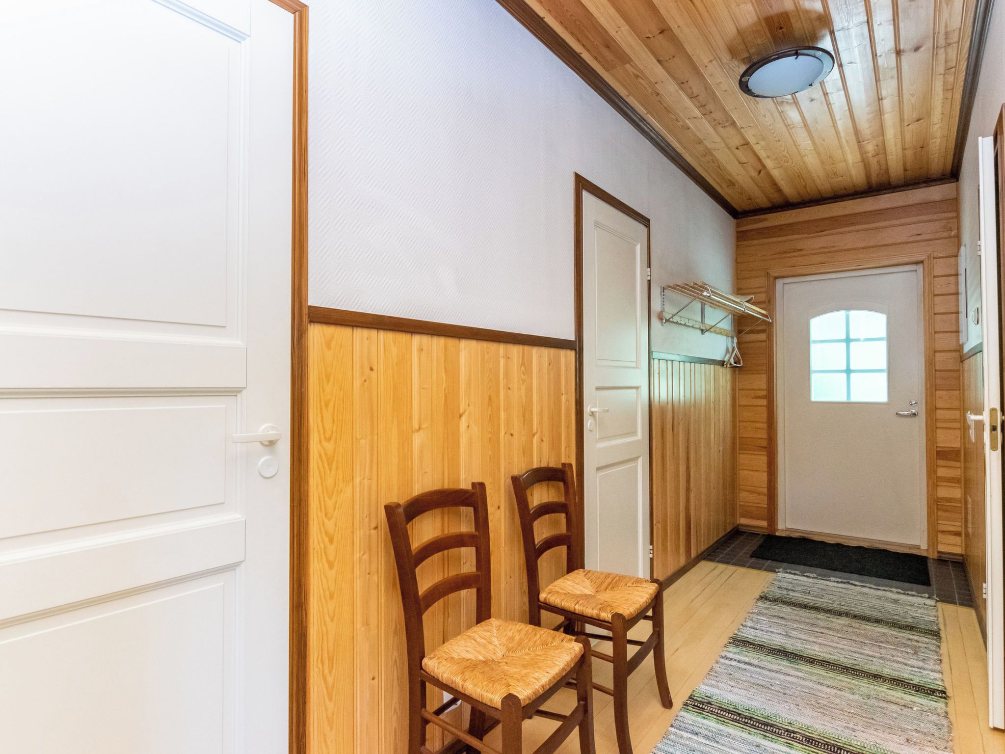 Un corridoio con pareti in legno, due sedie di legno, una porta con finestra e un lampadario.