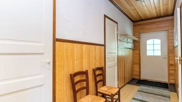 Ein Korridor mit Holzwänden, zwei Holzstühlen, einer Tür mit Fenster und einer Deckenleuchte.