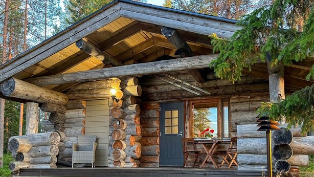 Une cabane en rondins avec un porche, un coin repas avec des chaises et une table, et une porte avec une fenêtre.