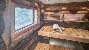 L’intérieur d’une cabane en rondins, avec un banc en bois, une fenêtre donnant sur les arbres et un plafond en pente.