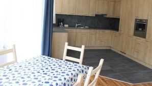 A compact kitchen with wooden cabinets, a black countertop, and a small dining area with a table and chairs. - Weideli by Interhome (Saas-Grund)