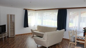 A living room with a sofa, a TV, a cabinet, and a dining area with a table and chairs. - Weideli by Interhome (Saas-Grund)
