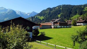 Un village rural avec des maisons traditionnelles, un champ verdoyant et des montagnes en arrière-plan.