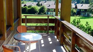 Un balcon avec une table et des chaises, donnant sur un quartier résidentiel avec des maisons et de la verdure.