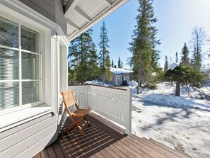 Une terrasse en bois avec une chaise, une balustrade blanche et une vue sur un paysage enneigé parsemé d’arbres.