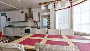 Une cuisine moderne avec des meubles blancs, une table à manger en bois agrémentée de sets de table rouges, des chaises en osier et des luminaires suspendus.